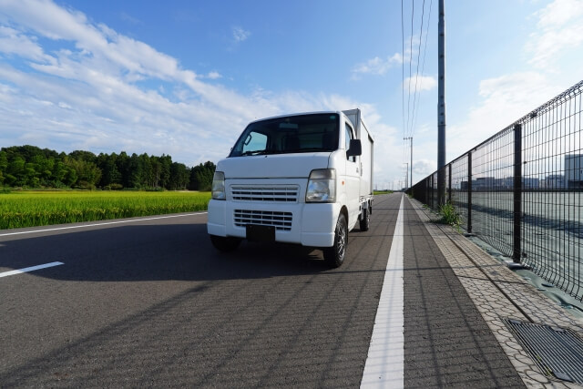 晴れた道を走る白い軽トラック