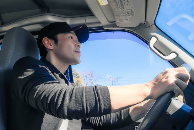 青空の下運転する若い男性ドライバー